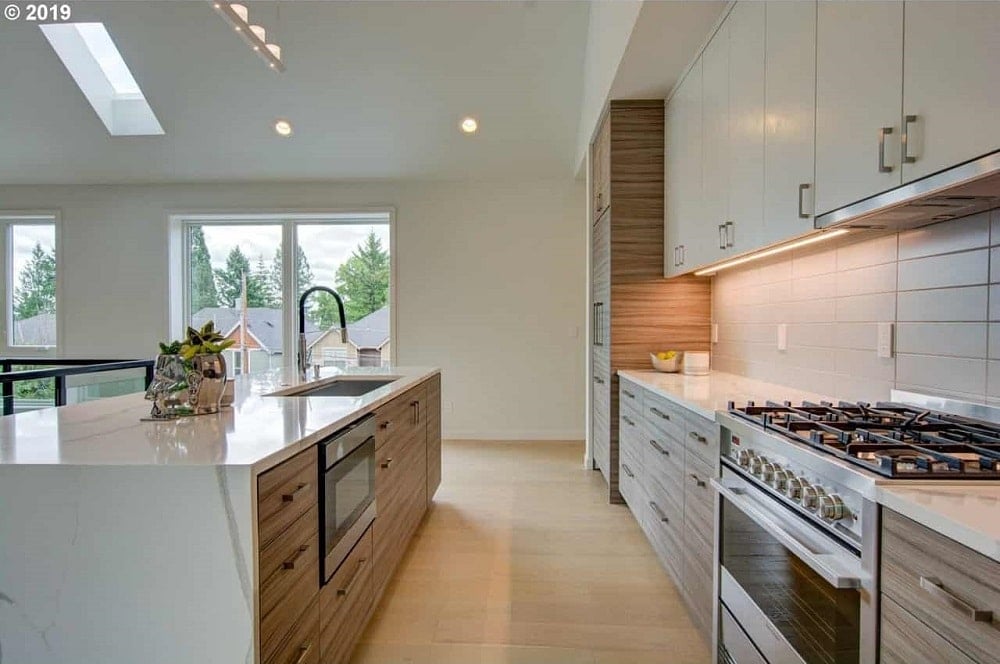 这是一个简单而可爱的狭长厨房，白色的台面与墙壁和高高的天花板很相配。它有棕色的橱柜，与硬木地板相匹配，与现代电器搭配得很好。