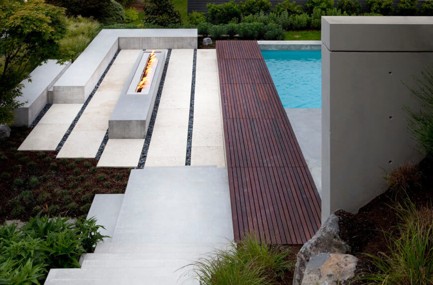 这个庭院提供丰富的木板，将固体场地一分为二。一种户外燃气壁炉条仍然横跨结构的游泳池，在左边。