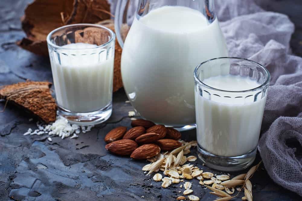 一罐牛奶夹在两杯牛奶之间，周围有各种坚果和一块布纱。