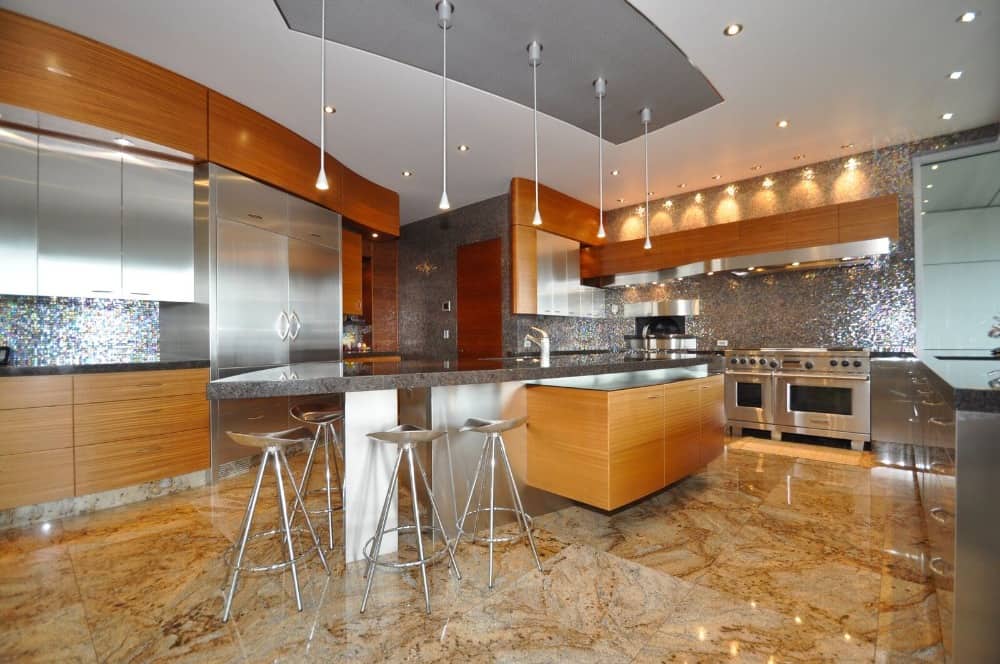 这间现代化的厨房配有豪华的不锈钢电器和米黄色的大理石地板。它有一个很大的厨房岛台，侧面有一个延伸部分，可以放置一张内置桌子，搭配现代风格的凳子。