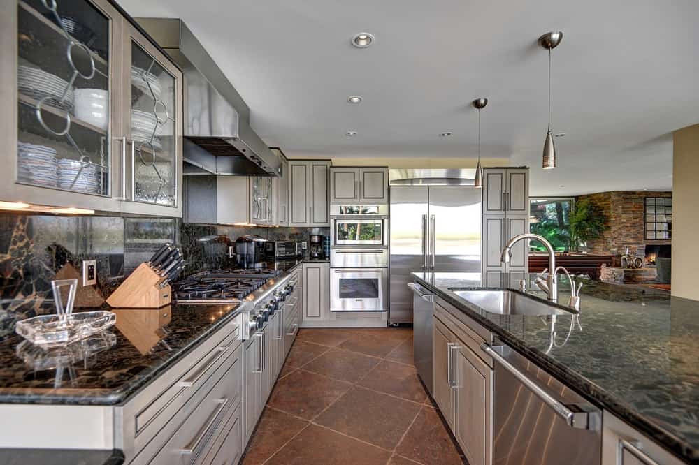 这是厨房风格的厨师厨房，深色花岗岩台面与不锈钢现代电器搭配得很好。这些是由迷人的陶土地板和白色天花板补充。