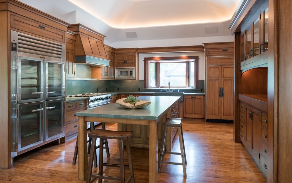 这间迷人的厨房有与橱柜相匹配的硬木地板。可爱的绿色台面与之相得益彰。中间的木制厨房岛台有一张附有木凳的桌子。