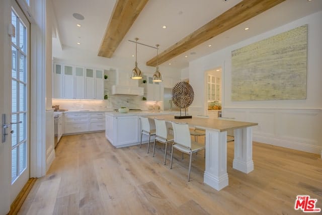 迷人厨房的这个角度有一张内置的木桌，连接到白色的厨房岛台。这张桌子与硬木地板和白色天花板的裸露横梁很好地融合在一起。