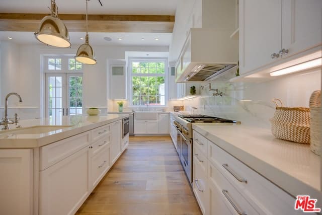 这间厨房狭长的硬木地板与经典的白色橱柜很好地搭配在一起，这些橱柜与装饰有外露横梁和吊灯的白色天花板很好地融合在一起。