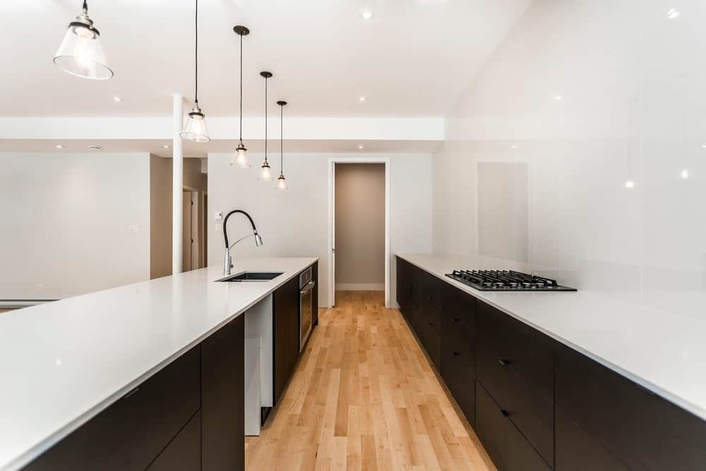 在这里，你可以看到狭长的厨房明亮的白色台面与黑色的现代橱柜形成对比。然后，这些顶部是吊灯，并辅以硬木地板。