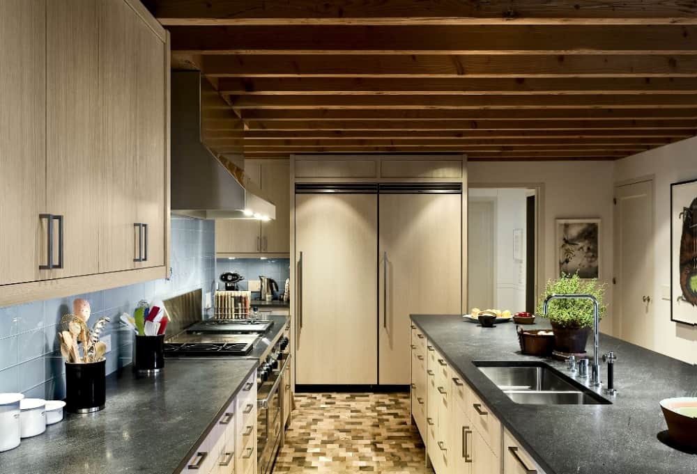 这是一个狭长的厨房，米黄色的橱柜与黑色的台面相辅相成，黑色的台面被天花板上的温暖灯光照亮。