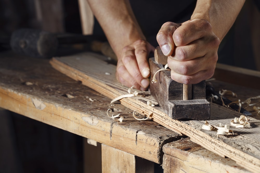 一个木匠用木刨刨木板的特写。