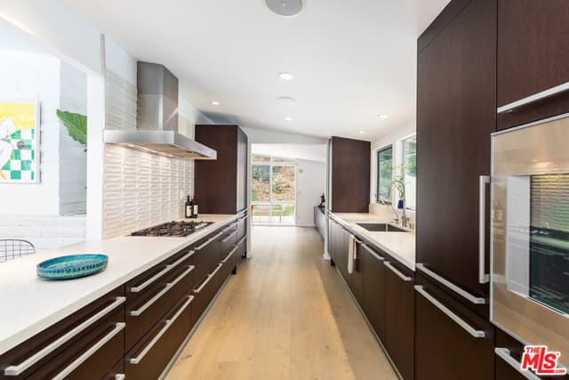 深棕色的现代橱柜在浅色硬木地板和白色棚顶的映衬下显得格外突出。这间狭长的厨房在烹饪区上方有一个不锈钢通风口。