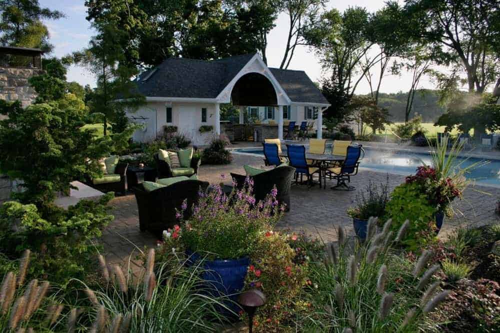 这是华丽的后院露台，通过陶土砖走道连接到泳池区域，过渡到华丽的周围花园的郁郁葱葱的景观。