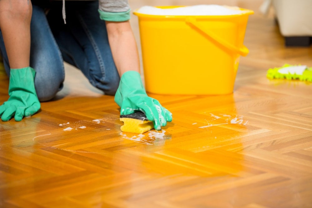 跪着用橡胶手套、海绵和一桶肥皂溶液清洁地板。
