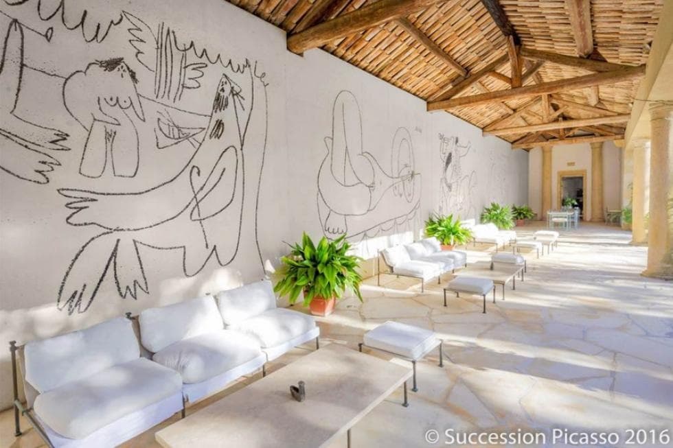 这是房子侧面的大型覆盖庭院，毕加索壁画装饰着巨大的白色墙壁。这为缓冲的沙发和大型咖啡桌制作了漂亮的背景，这些桌子与面积的米色底板与木制天花板一起混合。图片礼貌的拓展REALESTATEDEALS.com。