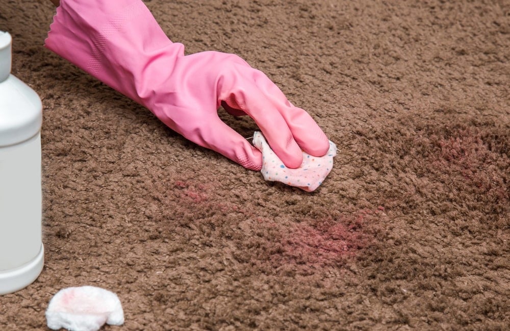 一只戴着手套的手正在清洗棕色地毯上的指甲油。