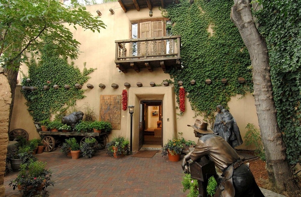 这是房子前面的景色，米黄色的墙壁上装饰着匍匐植物、雕像和各种植物，它们位于小木阳台下面的入口通道两侧。图片来自Toptenrealestatedeals.com。