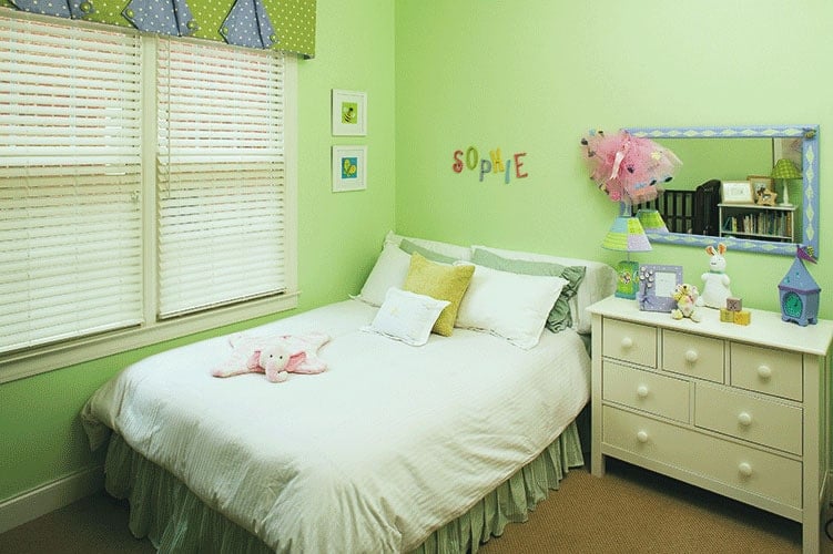 这间卧室铺着米黄色的地毯，亮绿色的墙壁上装饰着白色框框的艺术品和一面长方形的镜子。