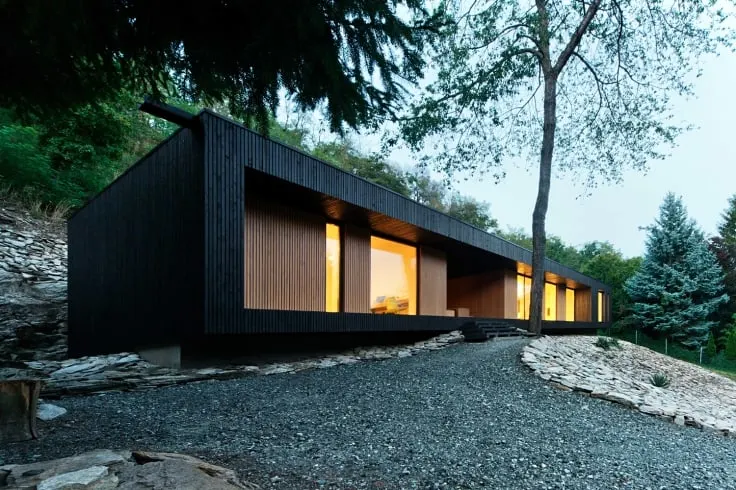 这是一个黑色的木制的房子外观。房子的房间有一个很好的氛围由于照明和岩石景观。