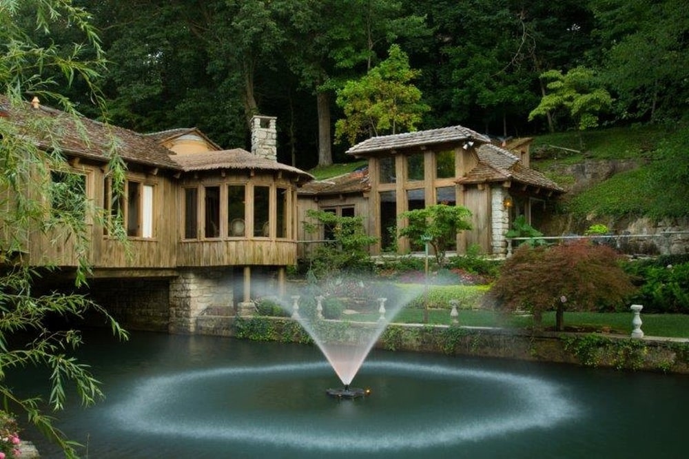 这是一栋前景有喷泉的房子。你可以在这里看到房子的木制外观，辅以高大的玻璃墙和高大的树木背景。图片来自Toptenrealestatedeals.com。