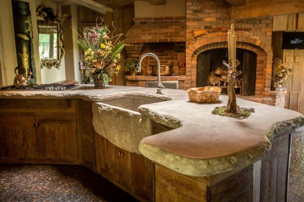 这是一个大弯曲的厨房岛台，它的石头台面有一个质朴的粗切设计，延伸到深深的水槽。图片来自Toptenrealestatedeals.com。