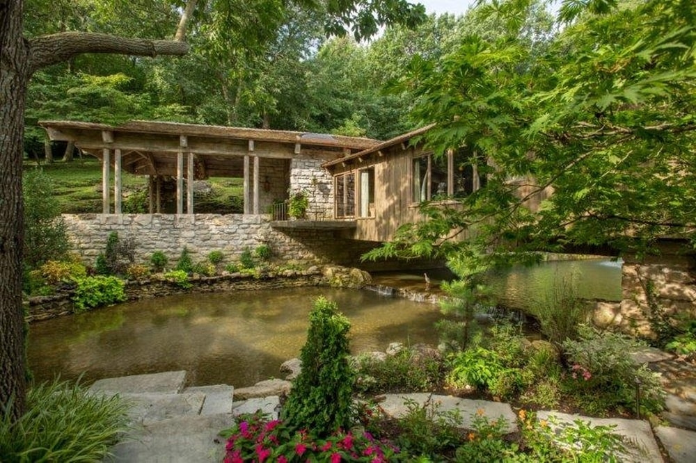 这是房子俯瞰的池塘的近景。周围环绕着五颜六色的开花灌木，装饰岩石和房子底部的石墙。图片来自Toptenrealestatedeals.com。
