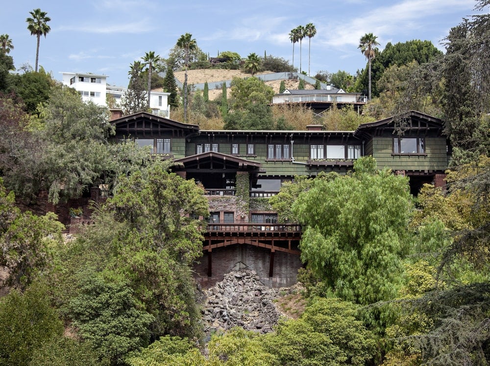 这是一个鸟瞰图的房子的后面看着好莱坞山的悬崖。你可以看到房子的暗色调外墙辅以周围高大的树木。图片由Toptenrealestatedeals.com。