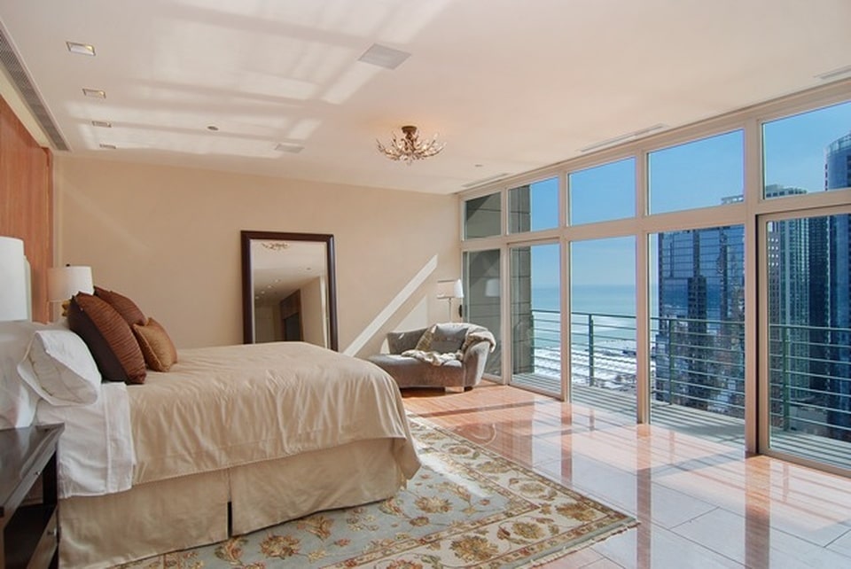 这间卧室里有一张米色的床，与米色的墙壁相匹配，米色的天花板被玻璃墙照亮。图片来自Toptenrealestatedeals.com。