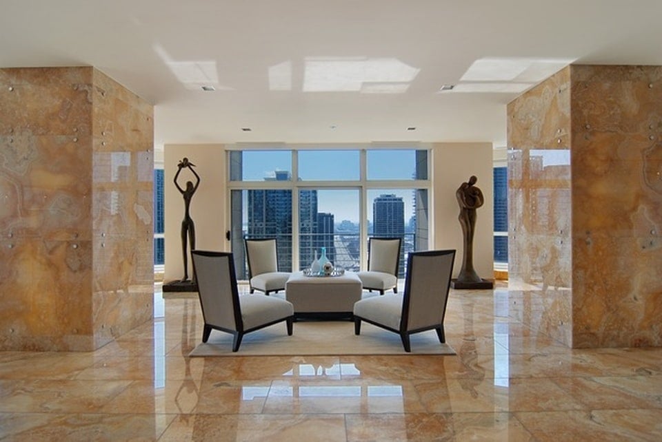 这是客厅和休息区，有灰色的椅子，米色的大理石地板和装饰着几尊雕像的柱子。图片来自Toptenrealestatedeals.com。