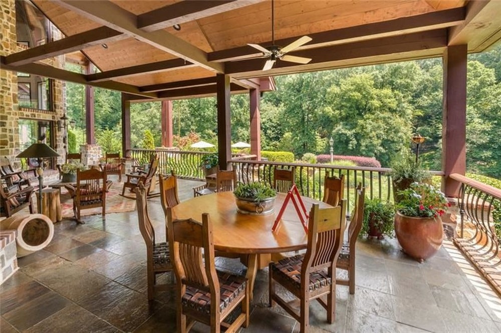 这是一个大露台，上面有一个木制的横梁天花板，室外餐厅配有木制桌椅，装饰着盆栽植物。图片来自Toptenrealestatedeals.com。