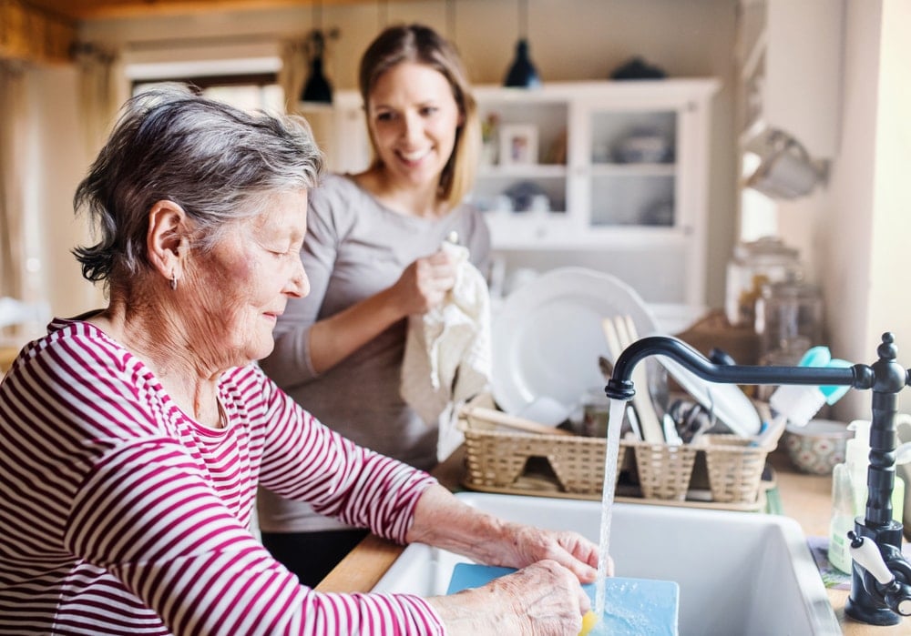 一位老妇人在洗盘子，一位年轻妇女在擦盘子。