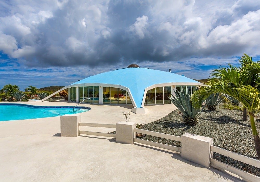 这是带有玻璃墙的圆顶房屋的正面视图。这与周围热带树木和大泳池的景观相辅相成。图片来自Toptenrealestatedeals.com。