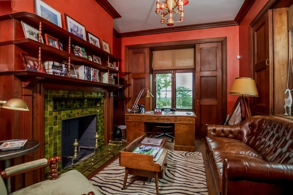 家庭办公室有充满活力的土红色墙壁，与深棕色色调相辅相成。你还可以看到沙发和壁炉彼此相对。图片来自Toptenrealestatedeals.com。