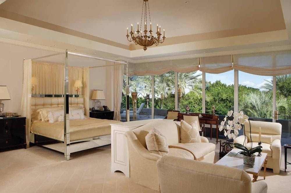 卧室里有一张镀铬的四柱床，与米色的墙壁、托盘天花板和床脚的沙发形成鲜明对比。图片来自Toptenrealestatedeals.com。
