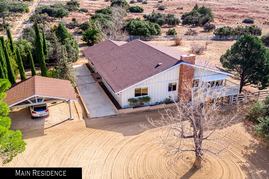 这是牧场主屋的鸟瞰图。它有白色的外墙和赤陶土屋顶，与周围点缀着灌木和树木的土地相匹配。图片来自Toptenrealestatedeals.com。