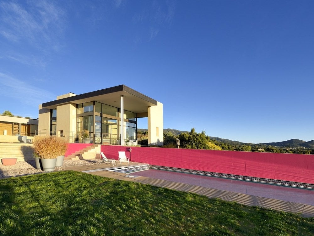 这是一个看当代房子大玻璃墙壁和柱子米色。你也可以在这里看到长长的粉色墙后院的游泳池旁边。图片由Toptenrealestatedeals.com。