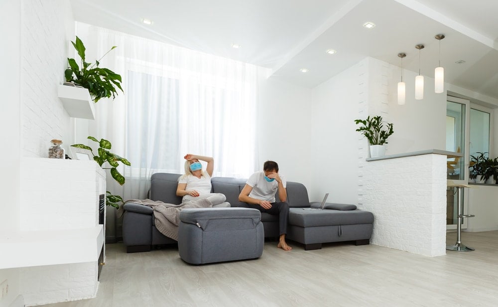 一对戴着口罩的夫妇坐在一间现代客厅的灰色沙发上。