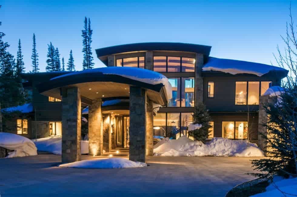 这是一个大型滑雪屋的正面视图，它有大型的石头结构，辅以丰富的玻璃墙，室内的温暖光线从中逃逸。