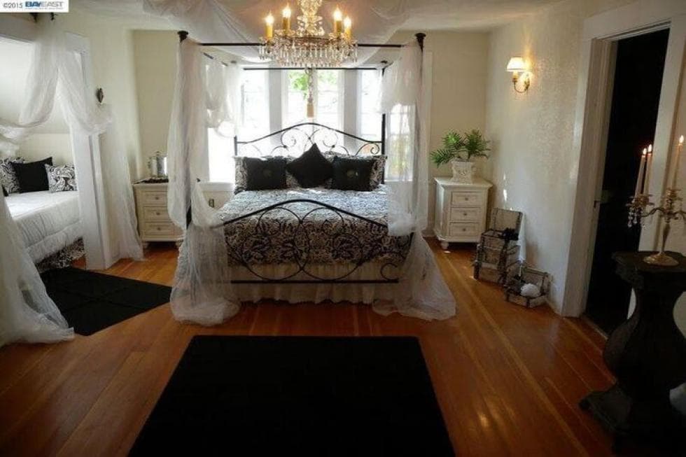 这间卧室里有一张锻铁的四柱床，床上的窗帘与浅色的墙壁和硬木地板搭配得很好。图片来自Toptenrealestatedeals.com。