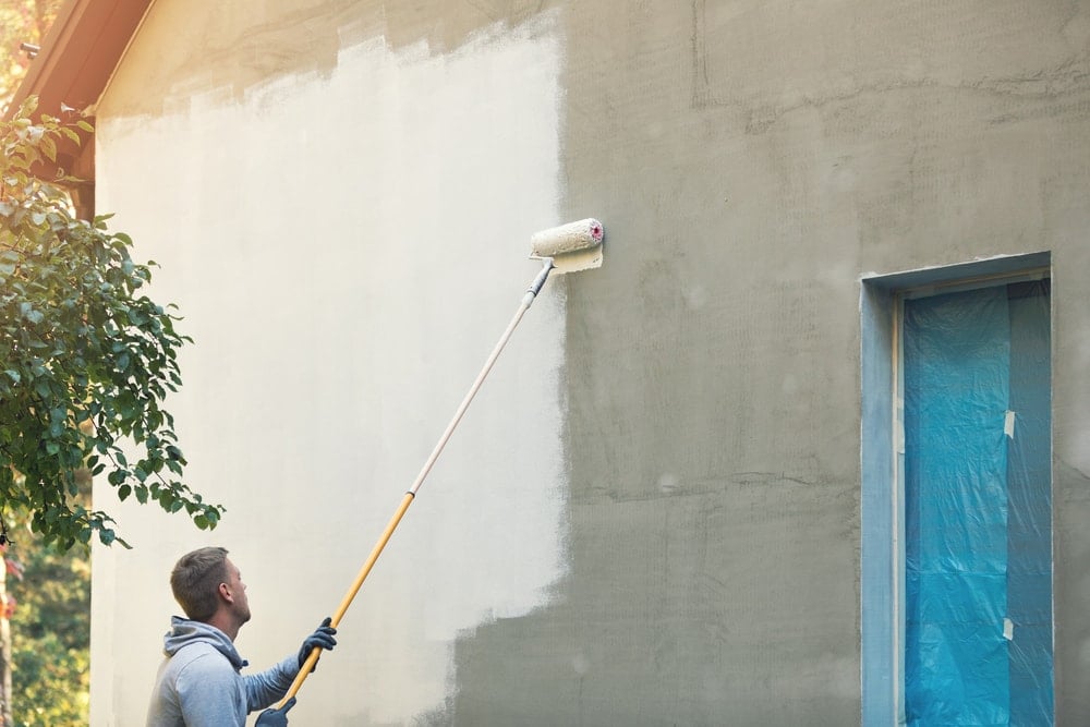 一名男子正在用压路机粉刷高高的混凝土外墙。