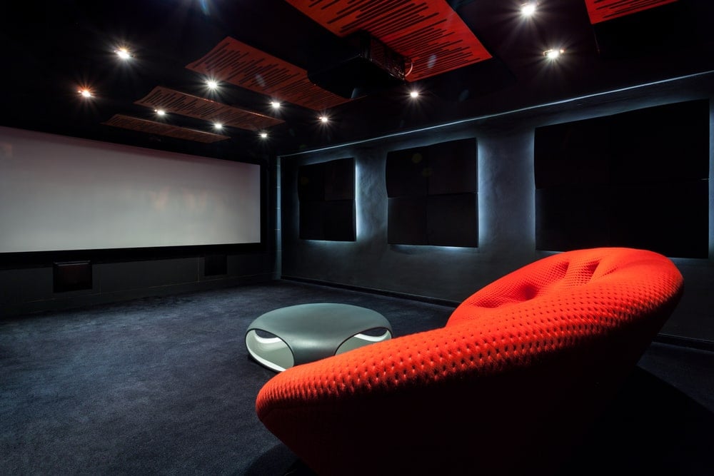 这是一个宽敞的家庭影院，有红色的沙发和远处的白色大屏幕。