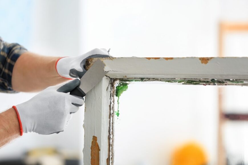仔细看看一名工人从旧窗框框架上刮掉涂料与油漆刮刀。