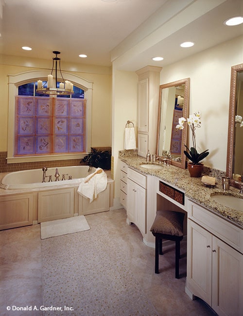 主浴室有圆形吊灯，双洗手池梳妆台和固定在拱形窗户下的落地式浴缸。
