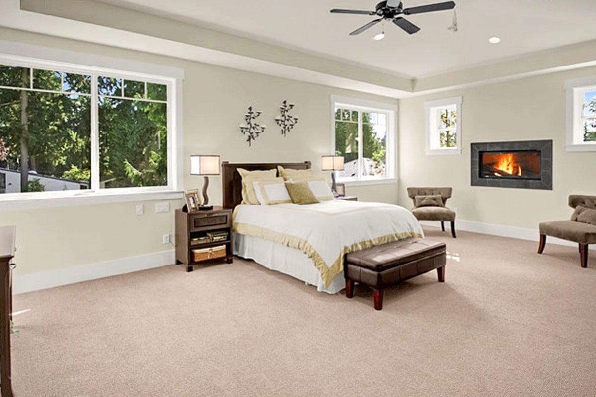 主卧室里有一座现代化的壁炉，棕色的靠背椅，还有一张裙摆床，床的一端是皮质的簇绒靠垫。