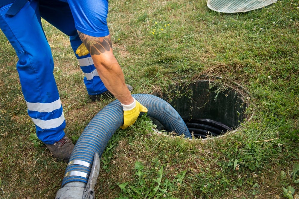 一名工人正在用一根粗的吸水软管清空地下化粪池。