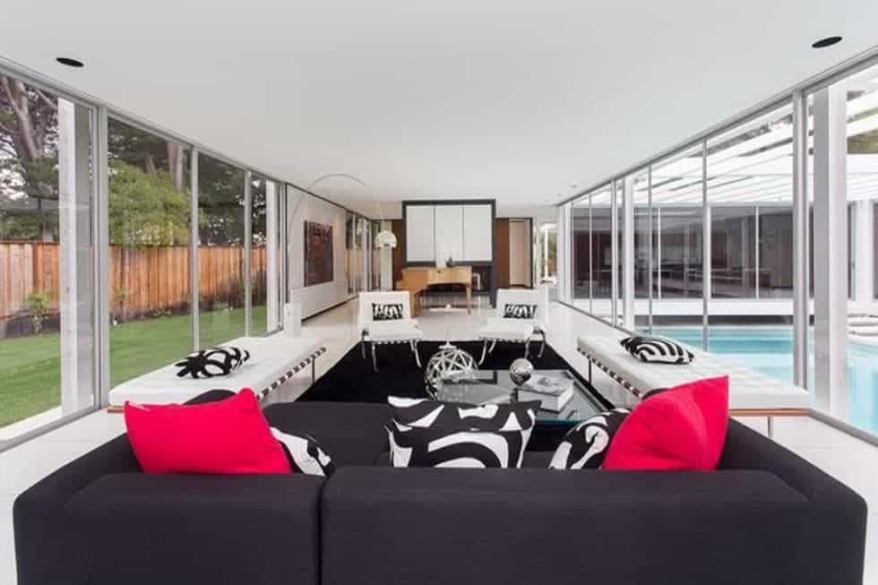 客厅里有一张深色沙发和一套白色家具，与黑色地毯形成对比。两侧的玻璃墙作为补充。图片来自Toptenrealestatedeals.com。