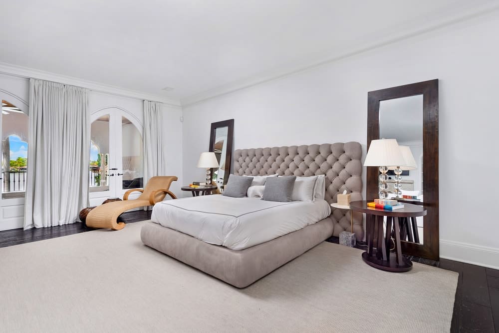 这个卧室有一个灰色的簇绒床两侧床头柜,大镜子和台灯。图片由Toptenrealestatedeals.com。
