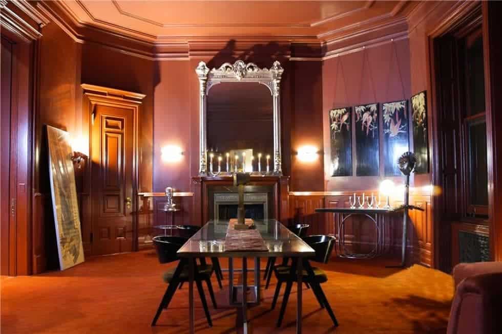 这是一间正式的餐厅，墙壁是暗红色的，壁炉的壁炉位于玻璃面餐桌的上方，周围是黑色的椅子。图片来自Toptenrealestatedeals.com。