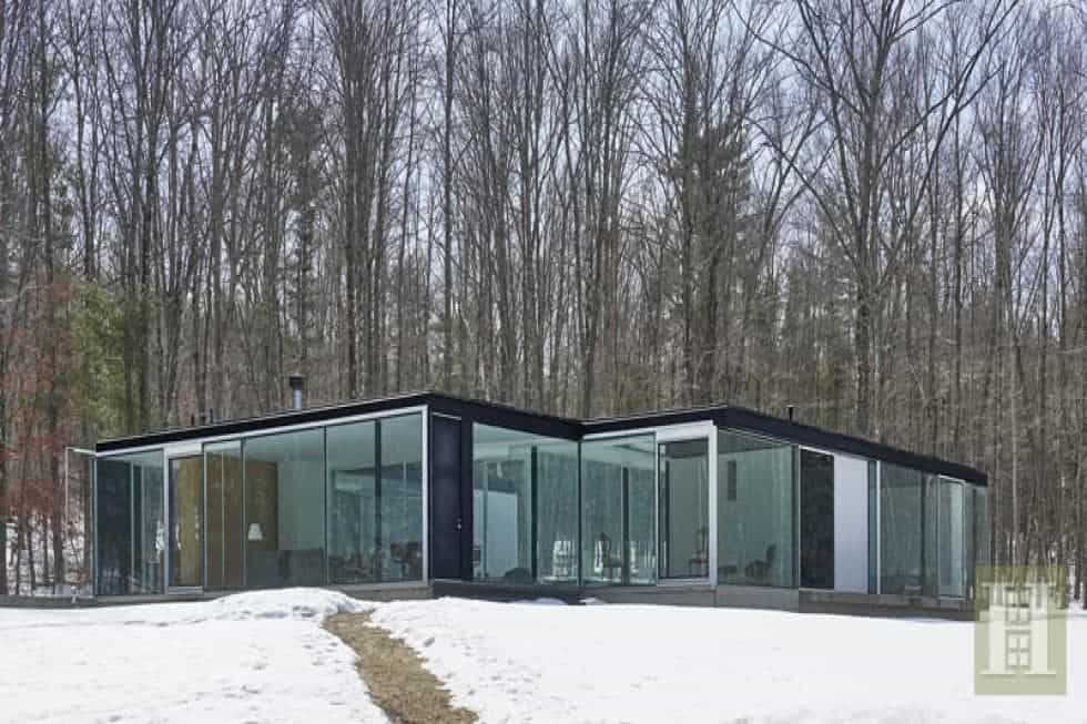 这是房子的外部视图，展示了它的玻璃墙，可以瞥见明亮的内部。周围的景观与之相得益彰。图片来自Toptenrealestatedeals.com。