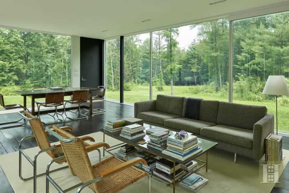 这是一个由玻璃墙包围的大型开放式房间中的客厅和用餐区。客厅区有一张灰色沙发，配上一张玻璃面咖啡桌和几把扶手椅。图片来自Toptenrealestatedeals.com。