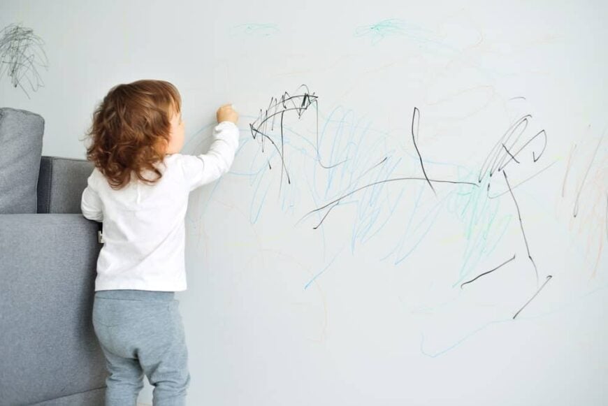 一个蹒跚学步的孩子在墙上玩蜡笔。