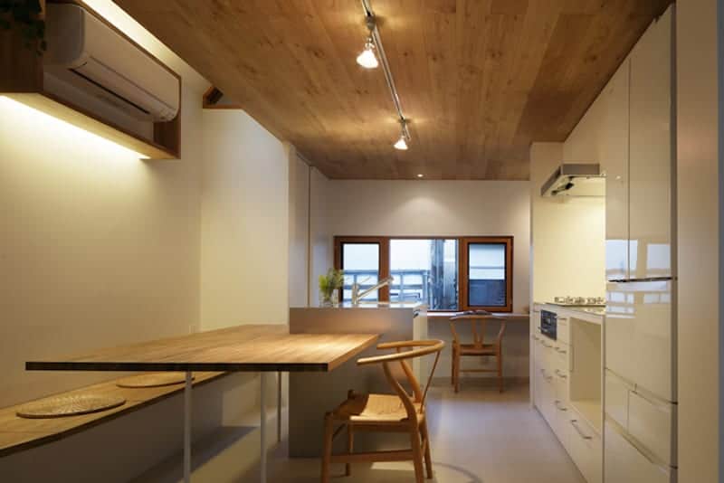 就餐式厨房的顶部是木质天花板，支持现代照明和射灯，照亮厨房和远侧的窗户。