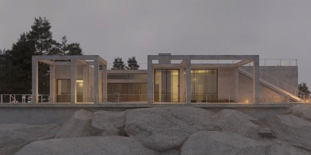 房屋的这一视图显示了支撑房屋基础的大岩石，房屋的浅米色外观通过温暖的室外灯光增强。