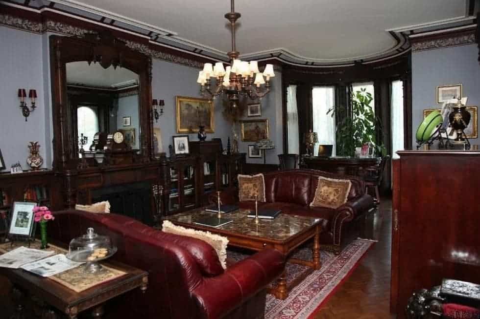 这间客厅里有几张深色皮沙发，两侧是一张木制咖啡桌，咖啡桌上方有一盏枝形吊灯，壁炉里有一个木制壁炉罩，可以取暖。图片来自Toptenrealestatedeals.com。